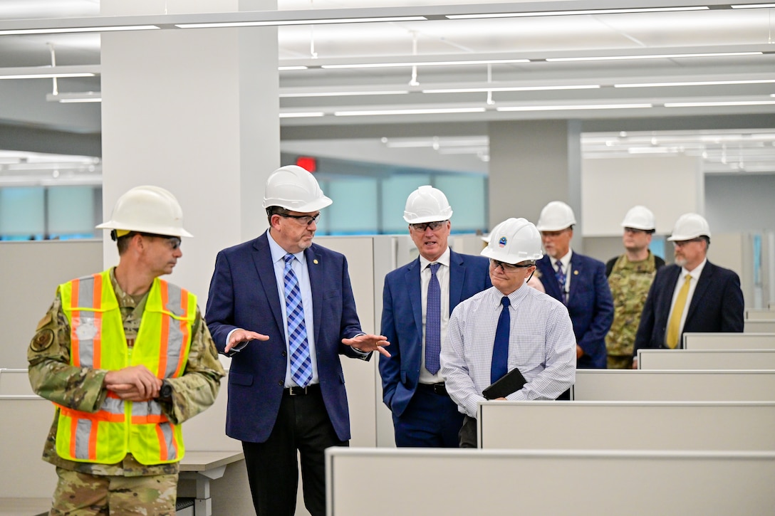 A group of people in hard hats tour a building with lots of cubicles
