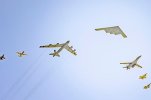 Seven different types of military aircraft fly overhead on a clear blue sky.