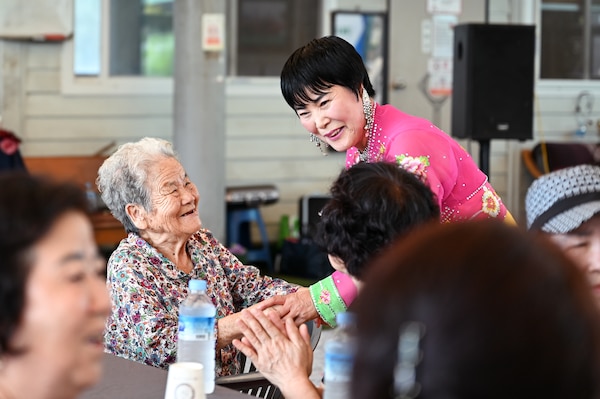 A singer in traditional dress greets a smiling senior citizen during the PTPI-hosted event, blending Korean cultural heritage and personal connection in the wake of recent regional floods.
