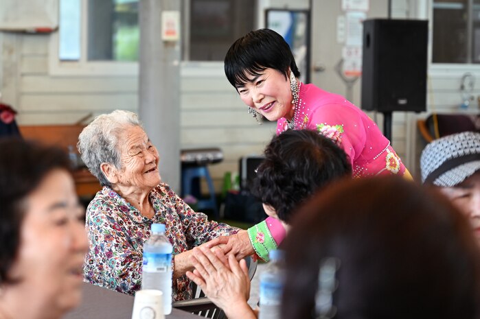 A singer in traditional dress greets a smiling senior citizen during the PTPI-hosted event, blending Korean cultural heritage and personal connection in the wake of recent regional floods.