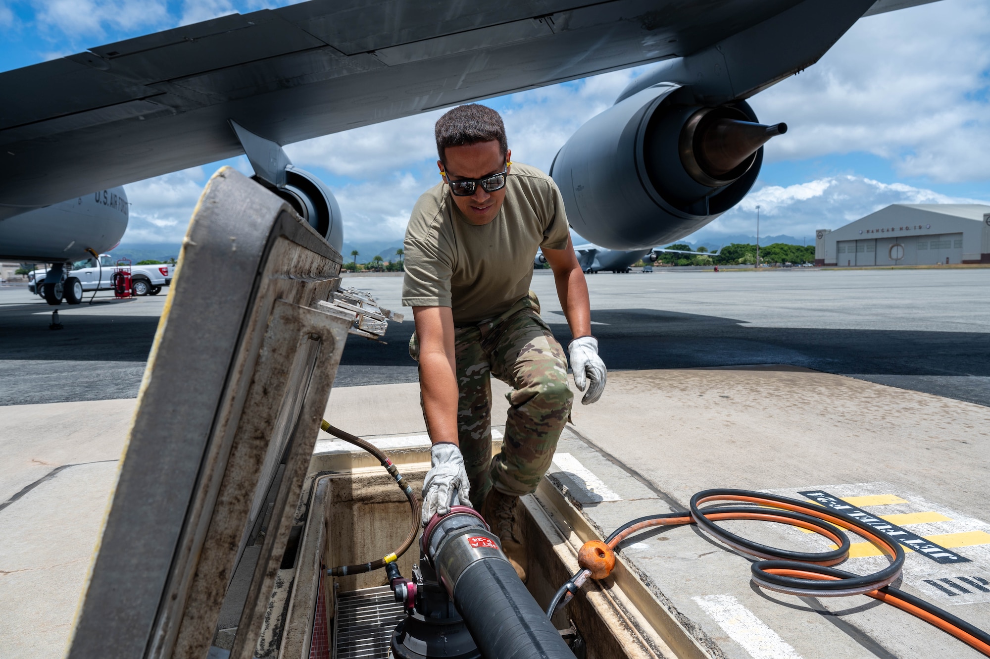 An Airman reaches into a fuel pit to prepare equipment to refuel an aircraft.