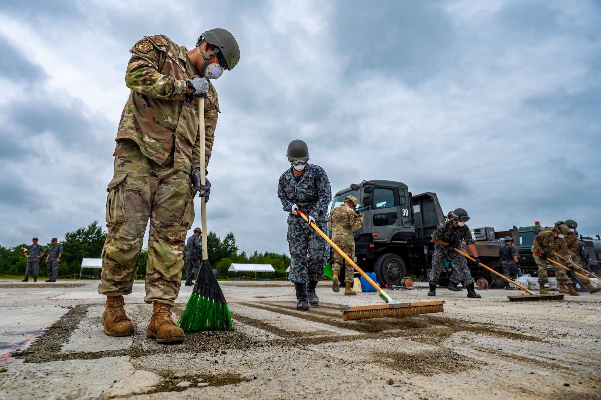 U.S. Air Force Airman 1st Class Michael Kowalski, left, 18th Civil Engineer Squadron heavy equipment operator, sweeps debris alongside a Japan Air Self Defense Force airmen assigned to the 2nd Air Wing during exercise Resolute Force Pacific 2025, while conducting Rapid Airfield Damage Repair (RADR) training at Chitose Air Base, Japan, July 29, 2025.
