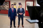 Two men stand next to each other in front of partially visible cameras and lights.