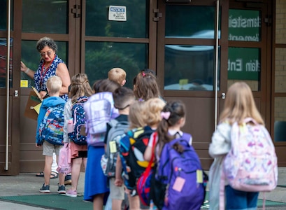 Female teacher leads a group of young students into school
