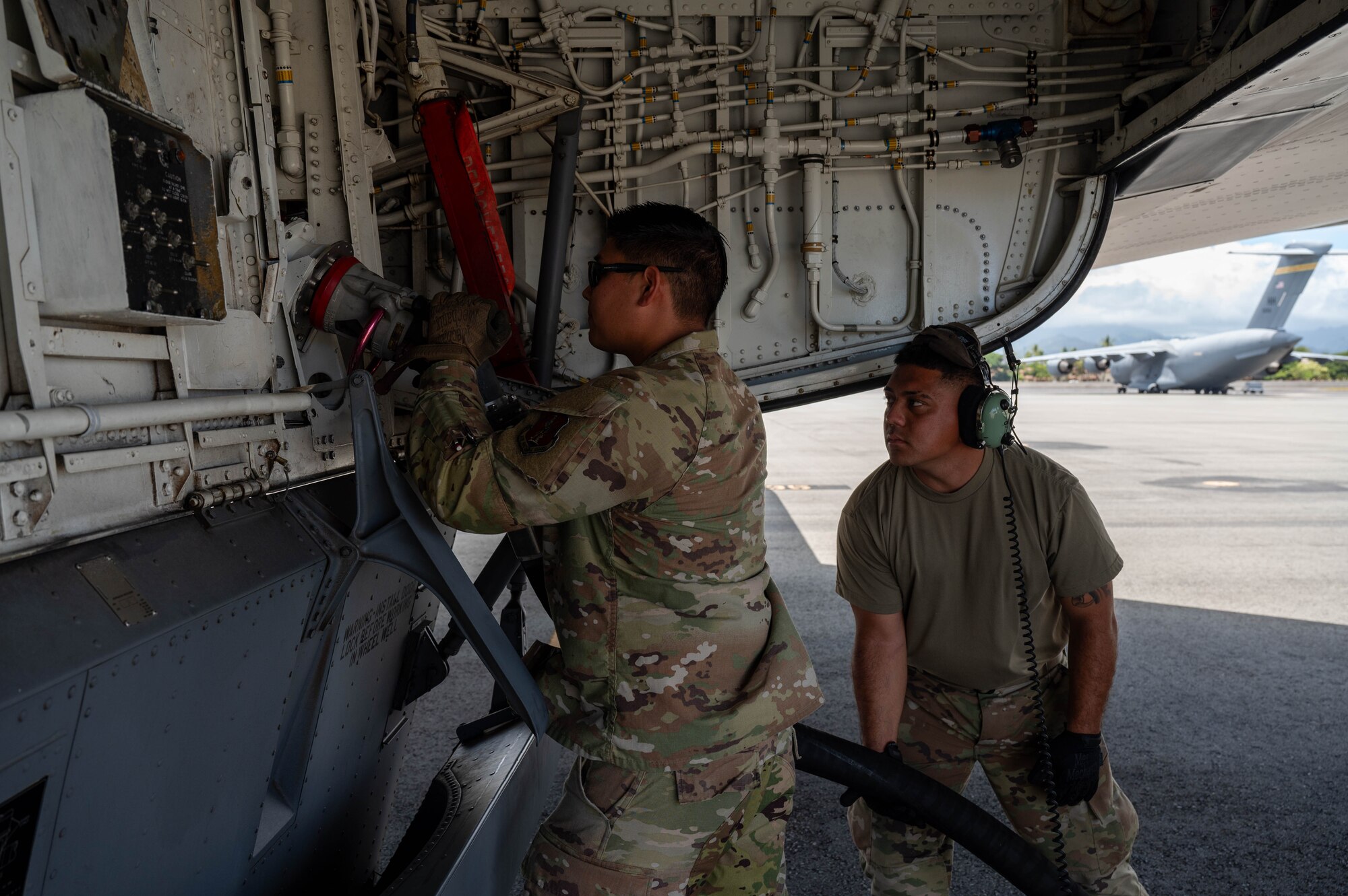 Two Airmen connect equipment to a KC-135 Stratotanker before refueling it.
