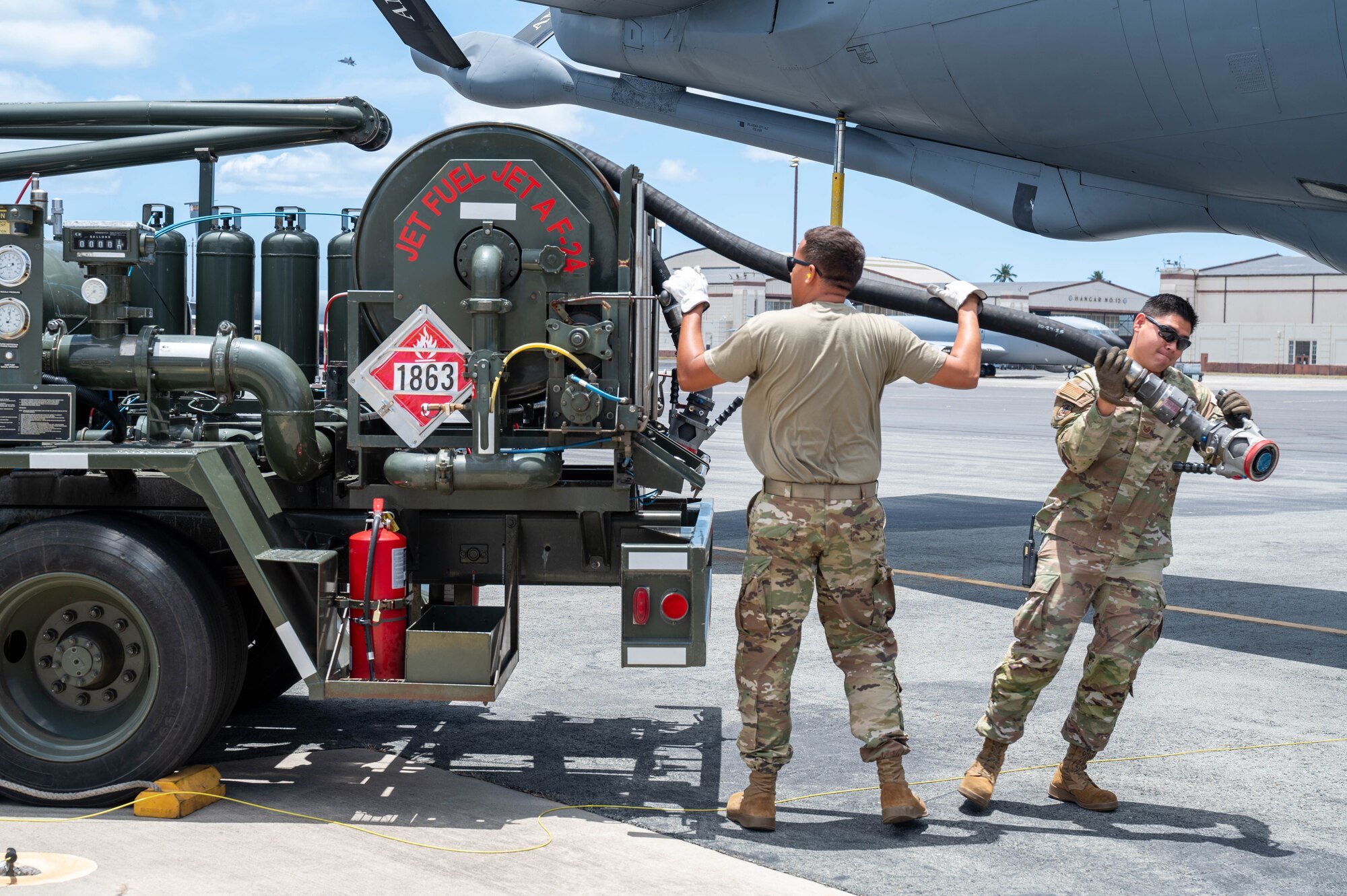 Two Airmen drag a hose from a fuel truck over to an aircraft before refueling it.