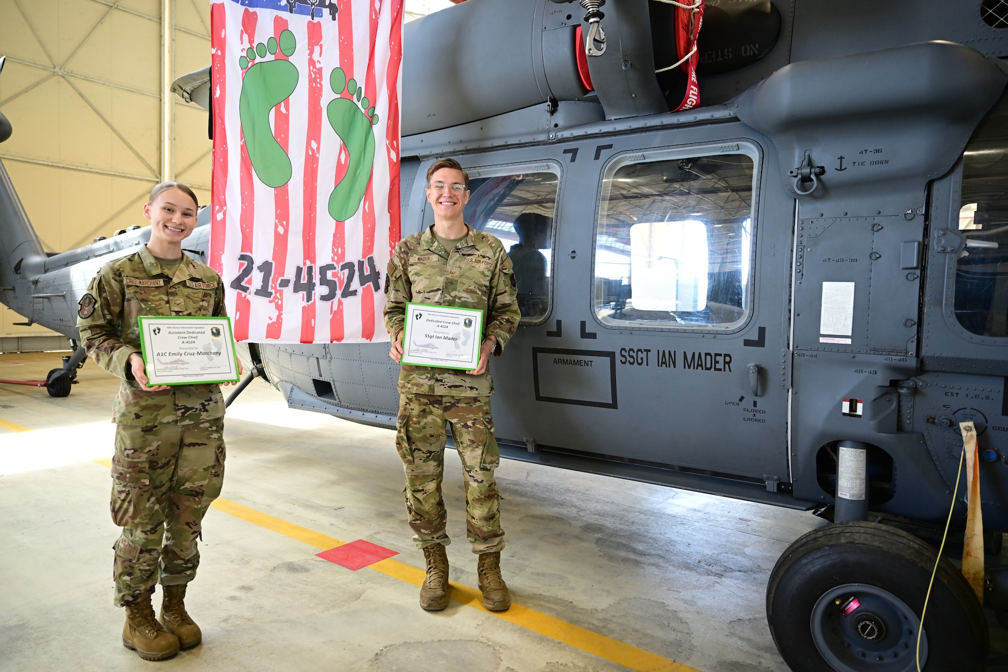 U.S. Air Force Airmen stand side by side in front of a helicopter.