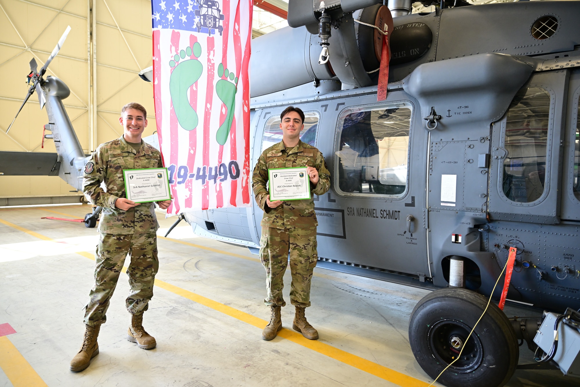 U.S. Air Force Airmen stand side by side in front of a helicopter.