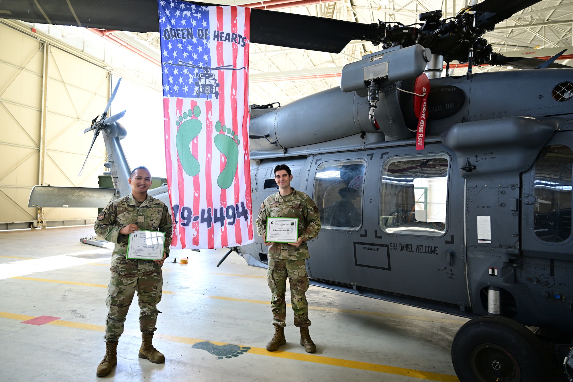 U.S. Air Force Airmen stand side by side in front of a helicopter.