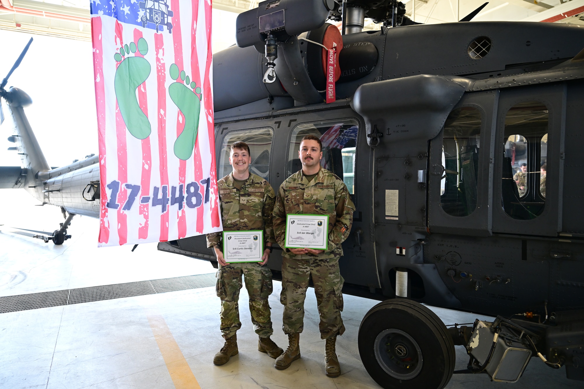 U.S. Air Force Airmen stand side by side in front of a helicopter.