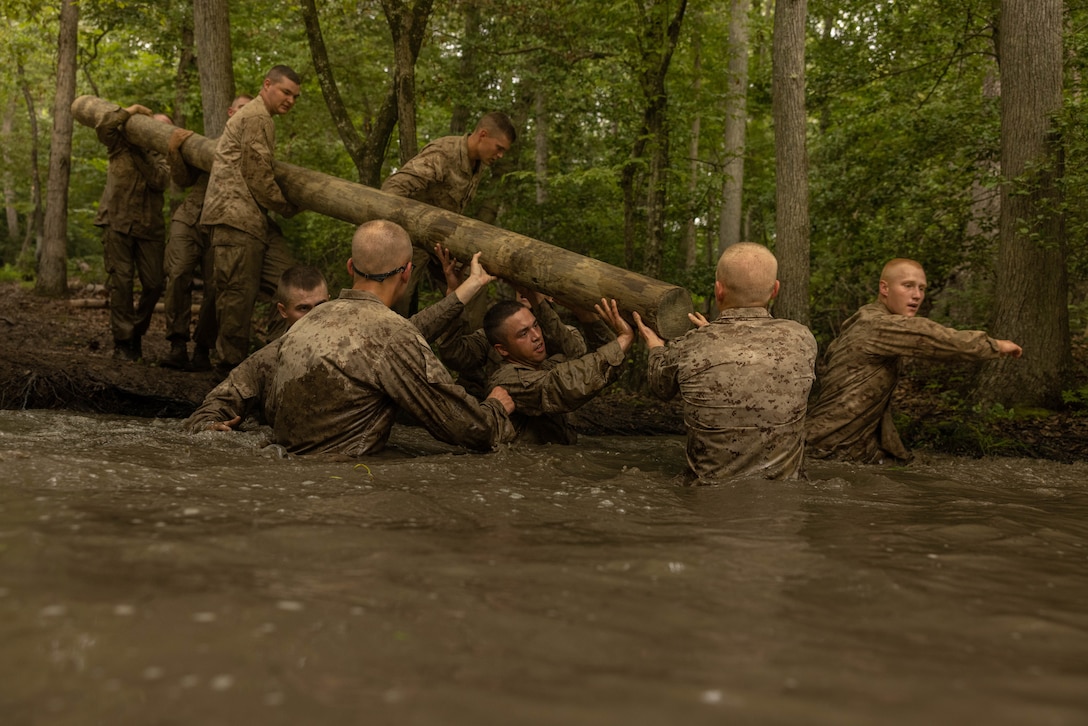 U.S. Marine Corps Officer Candidates with the Officer Candidate School carry a log through water while conducting the Montford Point Challenge at OCS on Marine Corps Base Quantico, Virginia, Aug. 5, 2025. Candidates, sergeant instructors, and physical training instructors completed the course in honor of the Montford Point Marines who were the first African Americans to enlist in the U.S. Marine Corps and further instilled the corps‘ warfighting mentality. (U.S. Marine Corps photo by Lance Cpl. Harleigh Faulk)
