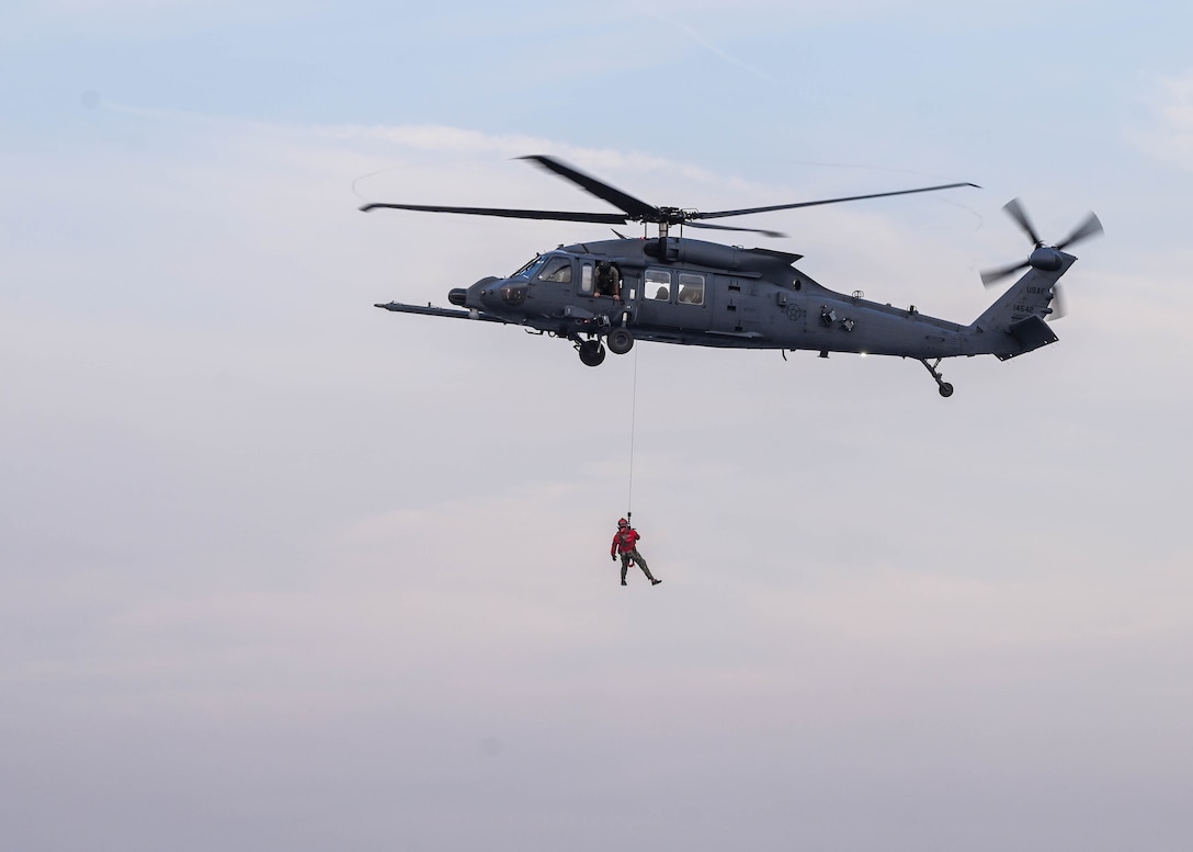 An airman in a harness hangs out of a helicopter in flight.