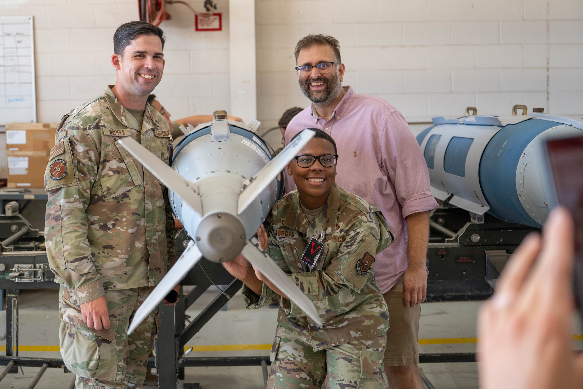 U.S Air Force Maj. Desiree Morgan, 7th Comptroller Squadron commander, and Master Sgt. Eric Whipple, 7th CPTS senior enlisted leader, pose for a photo with Mr. Amit Bhakta, 7th CPTS honorary commander, after assembling a Joint Direct Attack Munition during a tour at Dyess Air Force Base, Texas, Aug. 6, 2025. The Dyess Honorary Commander program strengthens local civic leaders understanding of the Air Force and defense missions. (U.S. Air Force photo by Airman Caleb Schellenberg)