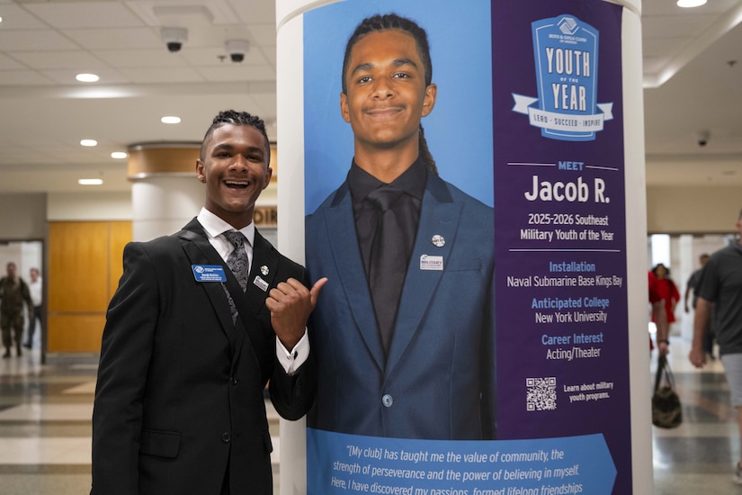 A young man stands near a column that features a poster with a photo of him, along with his name.