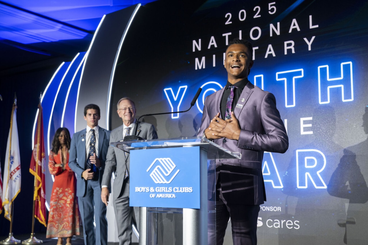 A young man stands behind a lectern that bears the logo of Boys and Girls Clubs of America. Behind him is a display screen that says "2025 National military youth of the Year."