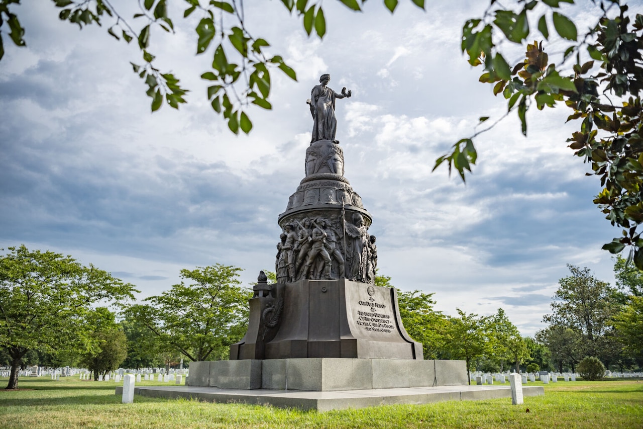 A large statue sits atop a pedestal amidst trees, greenery and grave stones.