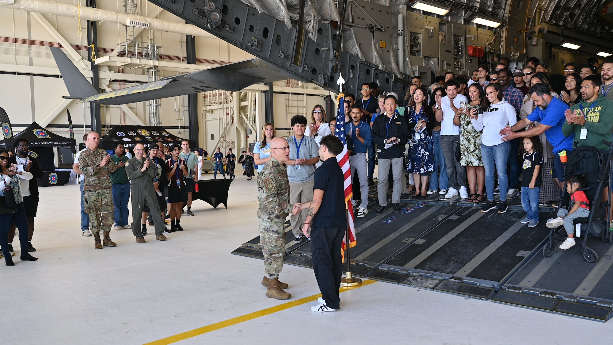 Col. Cade C. Gibson, commander of the 349th Maintenance Group, shakes hands with new recruit Shaun Ian Rodriguez following an oath of enlistment ceremony on the ramp of a C-17 Globemaster III at Travis Air Force Base, Calif., Aug. 3, 2025. Lt. Col. Dennis Hale, commander of the 349th Maintenance Support Group, and Col. Joseph Romeo, commander of the 349th Operations Group, join event attendees in applause to celebrate the start of Rodriguez’s career as a Reserve Airman. The Travis Air Reserve Experience is a recruiting event designed to give community members an opportunity to interact directly with Reserve Airmen, learn about career paths, and explore the mission of the 349th Air Mobility Wing.