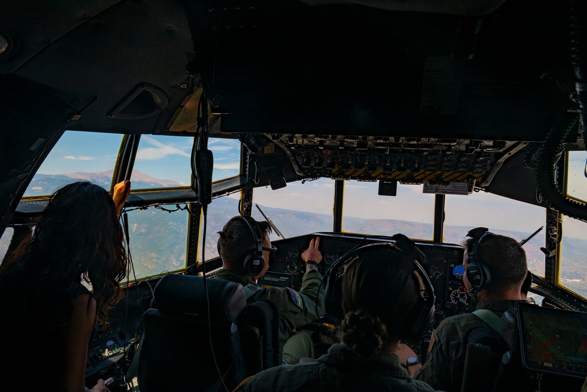 A woman in civilian clothes stands next to a crew of military aviators inside the crew compartment of a military aircraft.