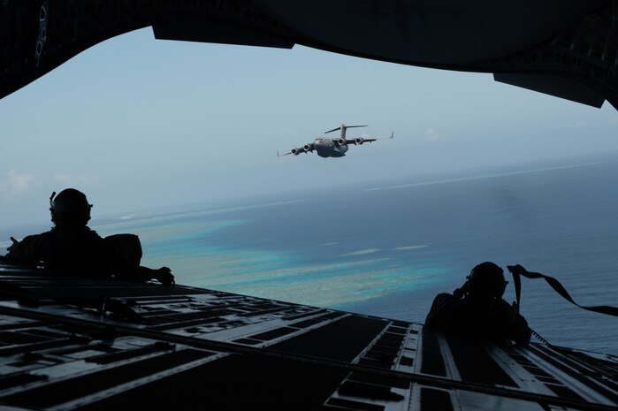 Two Airmen watch a C-17 Globemaster III fly from the back of another C-17 Globemaster III aircraft.