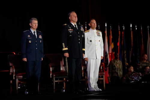 Chairman of the Joint Chiefs of Staff, U.S. Air Force Gen. Dan Caine, left, the outgoing commander of U.S. Central Command (USCENTCOM), U.S. Army Gen. Michael Erik Kurilla, center, and the incoming commander of USCENTCOM, U.S. Navy Adm. Brad Cooper, right, stand at attention at a change of command ceremony, 8 August 2025. Multiple Department of Defense officials attended the event as well as distinguished defense leaders from partner nations around the world. (U.S. Central Command Public Affairs photo by Tom Gagnier)