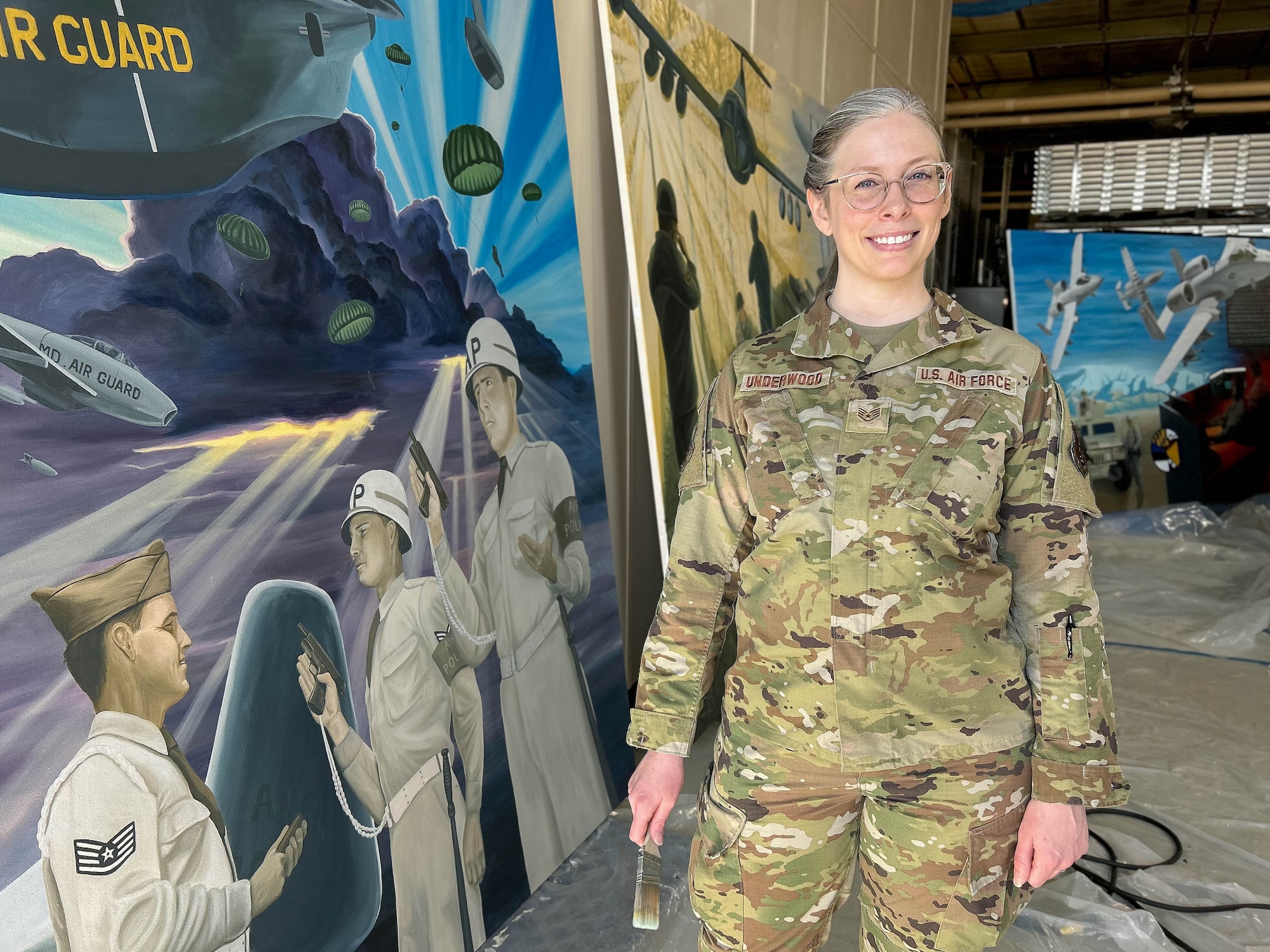 Maryland Air National Guard Staff Sgt. Rachel Underwood, public affairs specialist for the 175th Wing, poses for a photo in front of her in-progress acrylic mural at Warfield Air National Guard Base at Martin State Airport, Maryland, March 1, 2025.