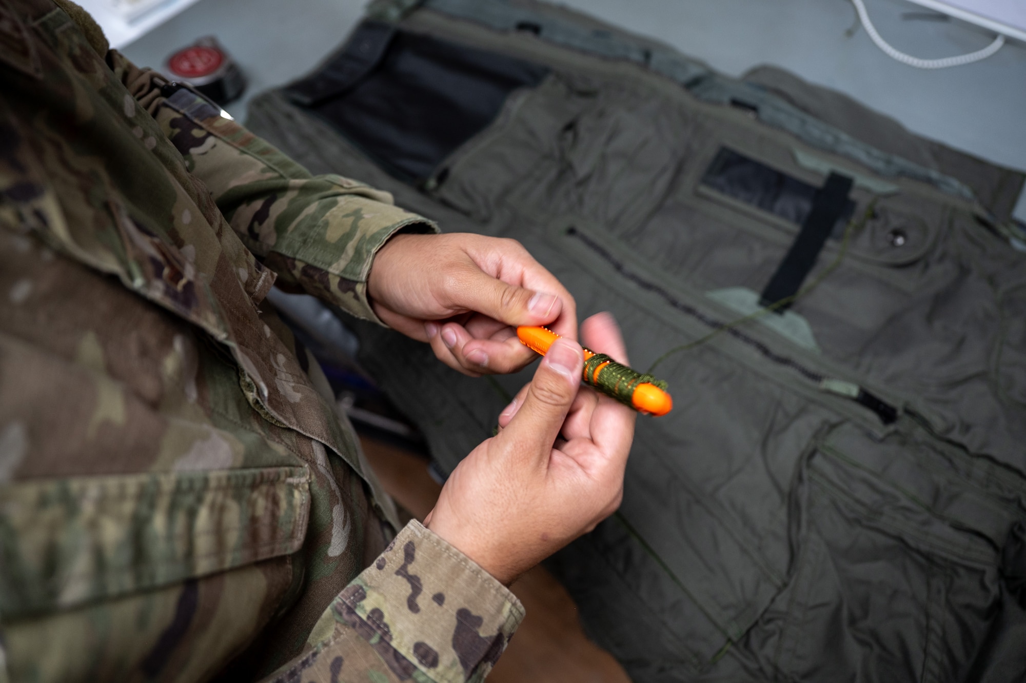 Airman winds paracord around a hook-blade knife attached to a pair of anti-g trousers