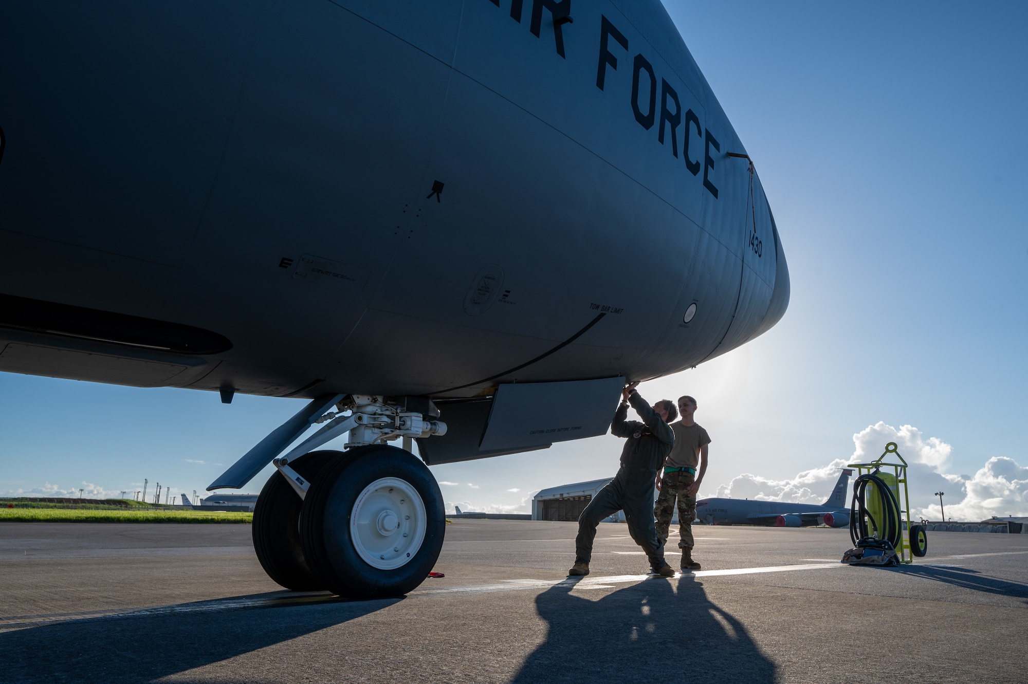 Two military members stand underneath a KC-135 Stratotanker to close the hatch next to the front wheel