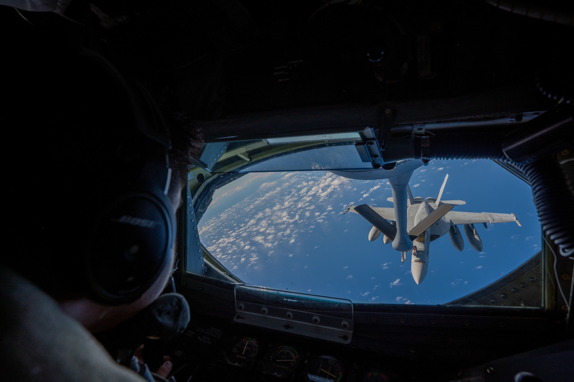 A military member lays on his stomach inside of the boom pod in front as he refuels and aircraft