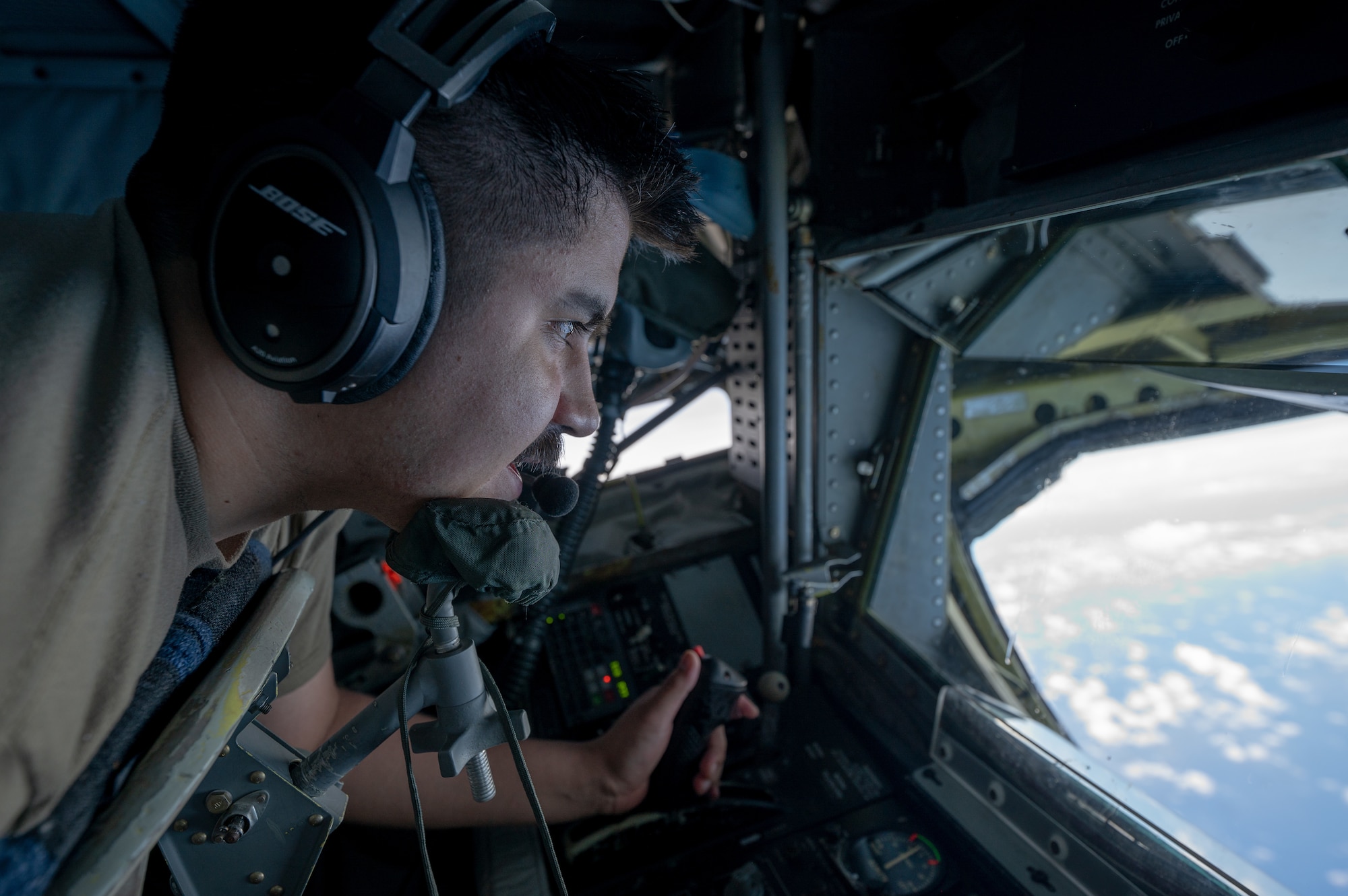 A military member lays on his stomach inside of the boom pod infront of a window to see a refueling