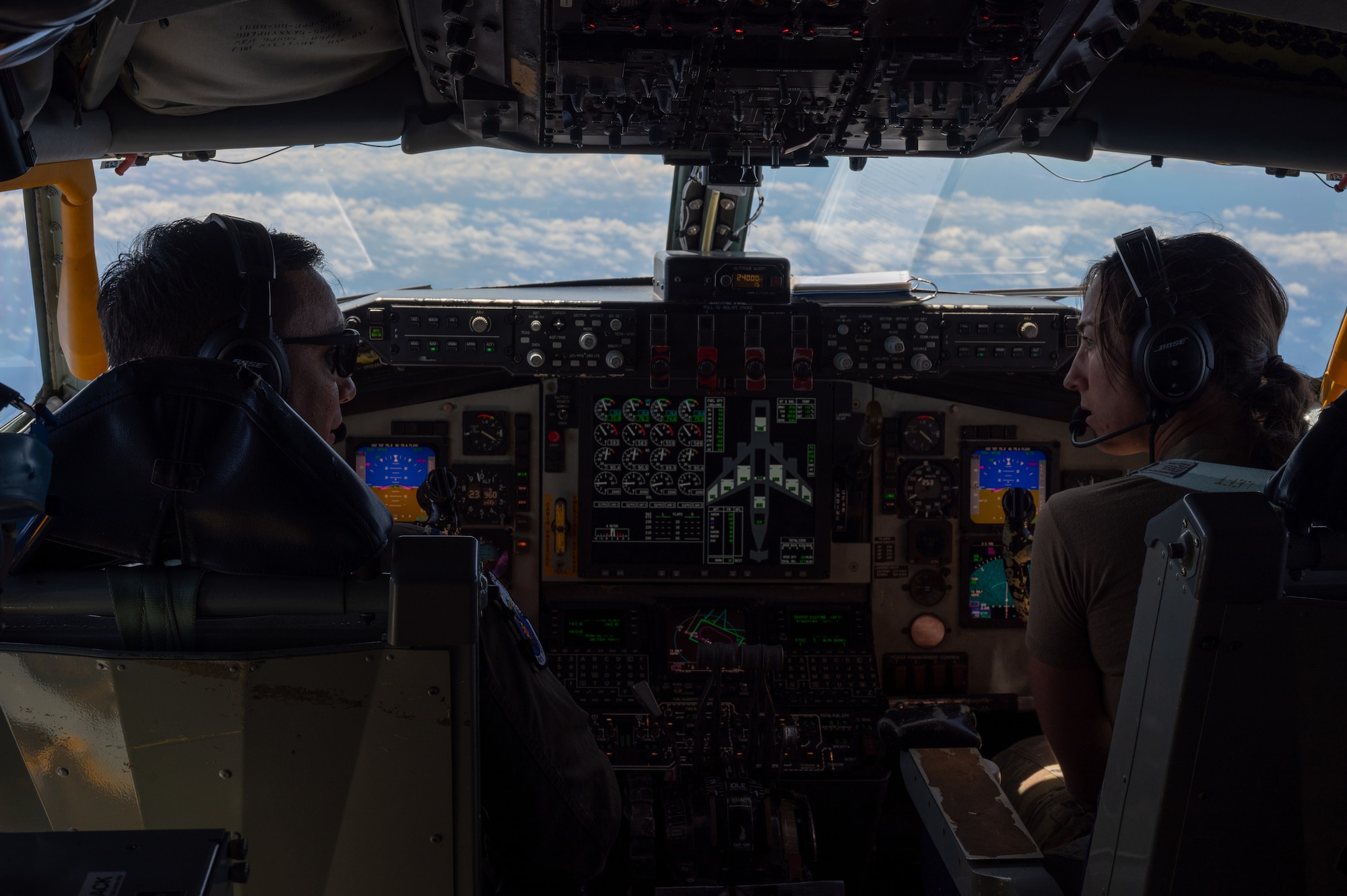 Two military pilots look at each other inside of a KC-135 aircraft while flying in the air
