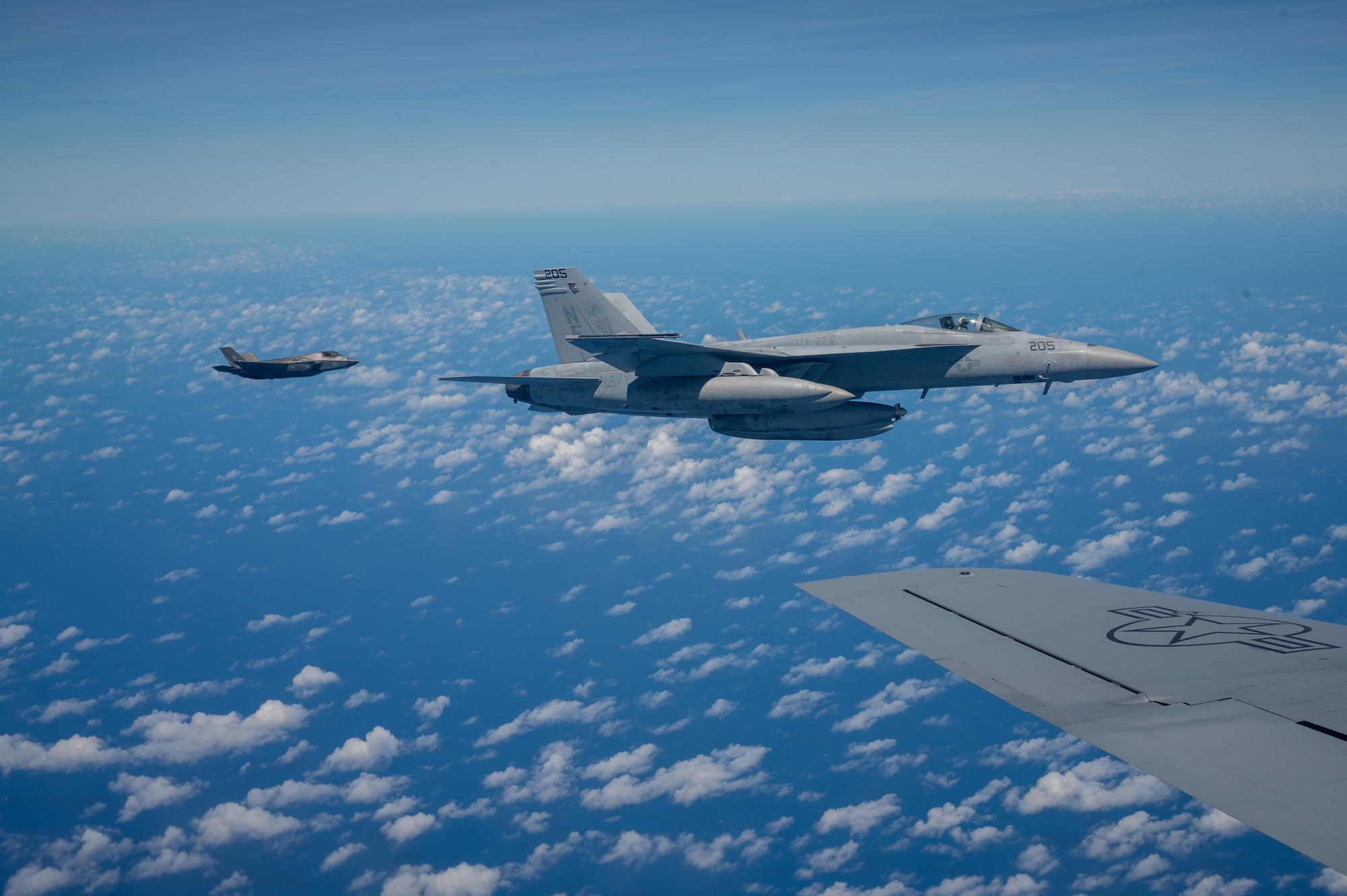 A F-35B aircraft flies behind a F-18 as it flies next to the wing of a KC-135 aircraft
