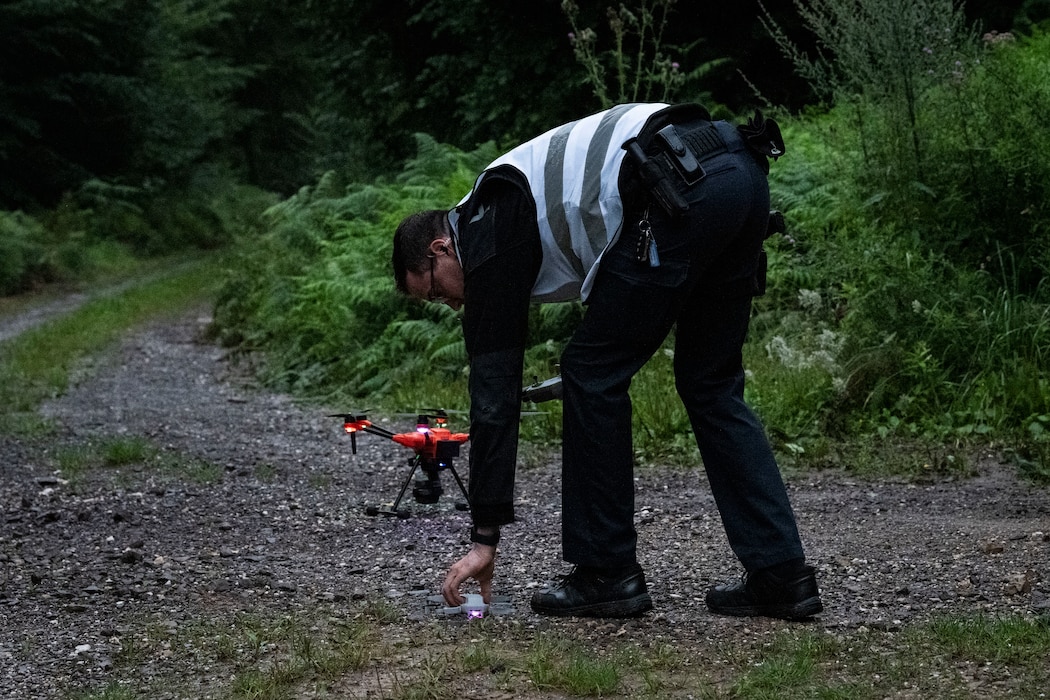 A policeman puts a drone on a wooded path