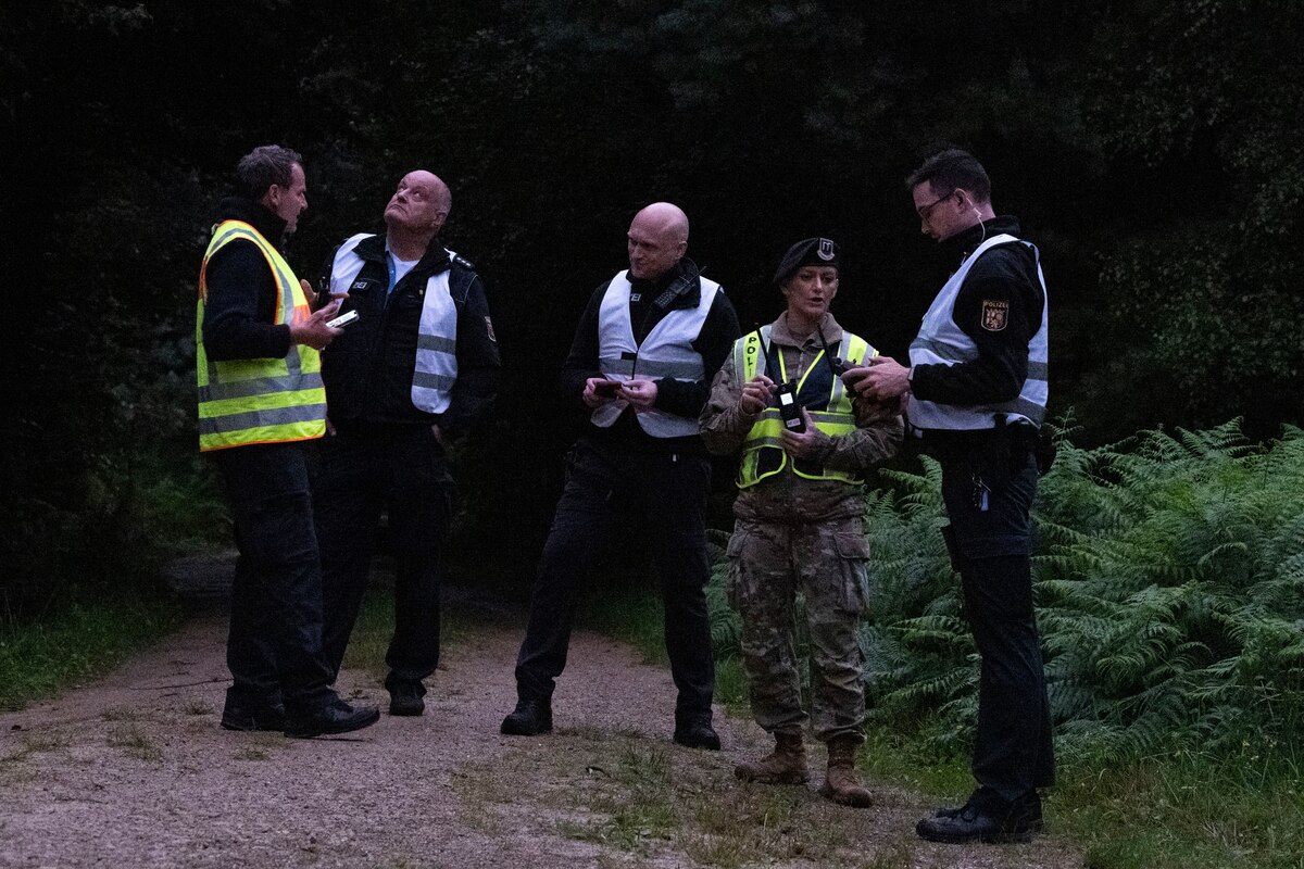 A group of military and civil police stand in a wooded path