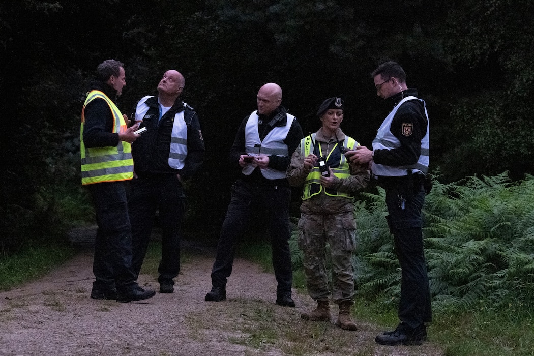 A group of military and civil police stand in a wooded path