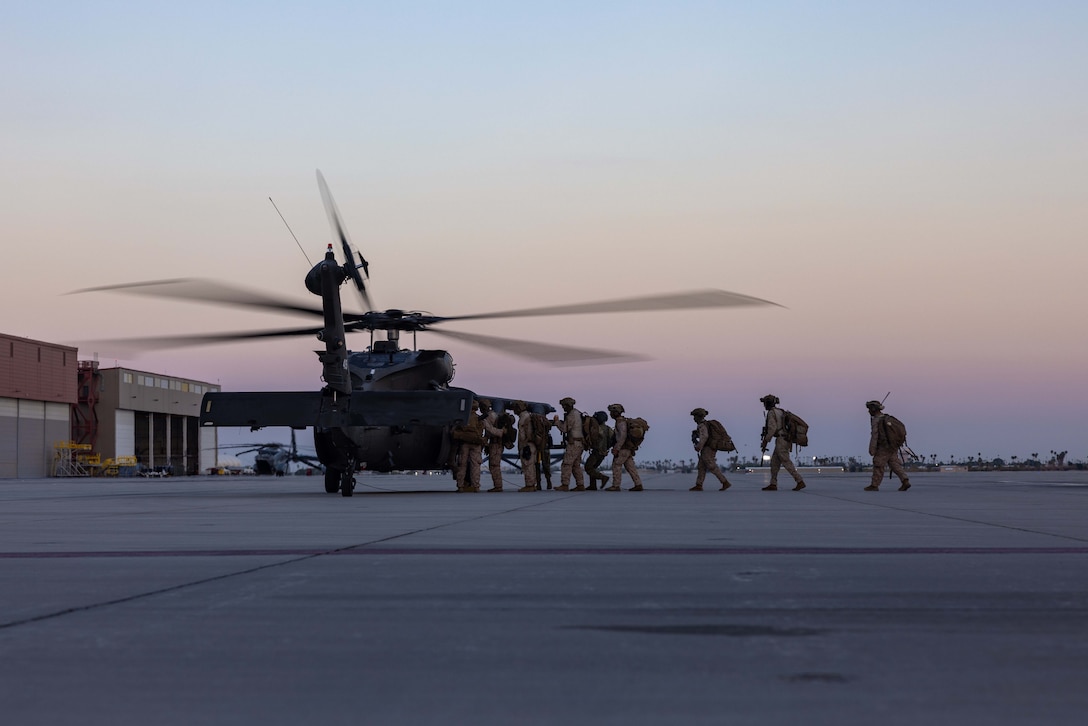 A group of Marines board a helicopter on a runway with a light purple sky behind.