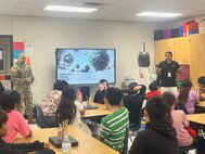 Capt. Jesus Silvas, a microbiologist with the U.S. Army Reserve Medical Command assigned to the 59th Medical Wing’s Office of Research and Technology Applications, and Dr. Israel Guerrero, a virologist with Texas Biomedical Research Institute, speak to students Aug. 7, 2025, at Mendez Elementary School in San Marcos, Texas
