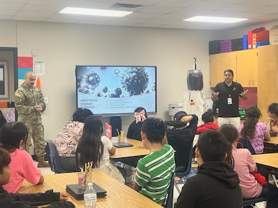 Capt. Jesus Silvas, a microbiologist with the U.S. Army Reserve Medical Command assigned to the 59th Medical Wing’s Office of Research and Technology Applications, and Dr. Israel Guerrero, a virologist with Texas Biomedical Research Institute, speak to students Aug. 7, 2025, at Mendez Elementary School in San Marcos, Texas