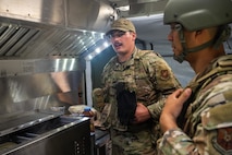 U.S. Air Force Staff Sgt. Chas Hunniford, 21st Combat Air Base Squadron fitness program manager, showcases an expandable single pallet expeditionary kitchen at a forward operating site during exercise Bamboo Eagle 25-3 at Camp Robinson, Arkansas, August 3, 2025. The ESPEK provides a fully functioning kitchen to support food service operations in forward-deployed environments. (U.S. Air Force photo by Airman 1st Class Adrien Tran)