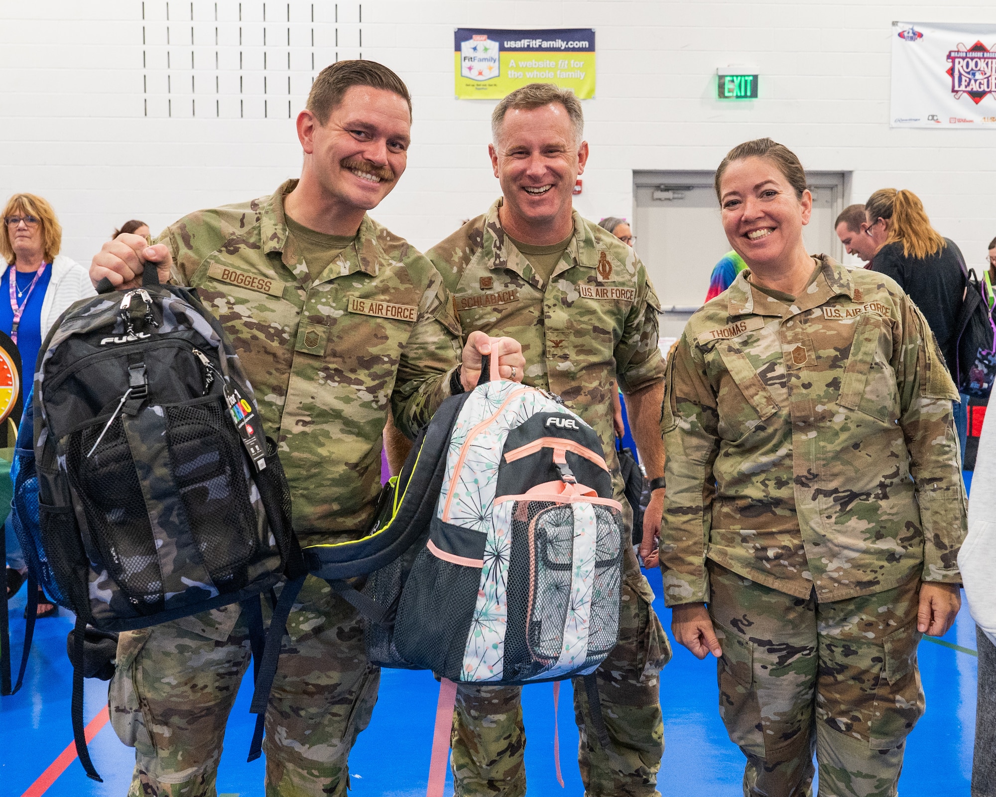 Three Airmen pose for a photo while holding backpacks.