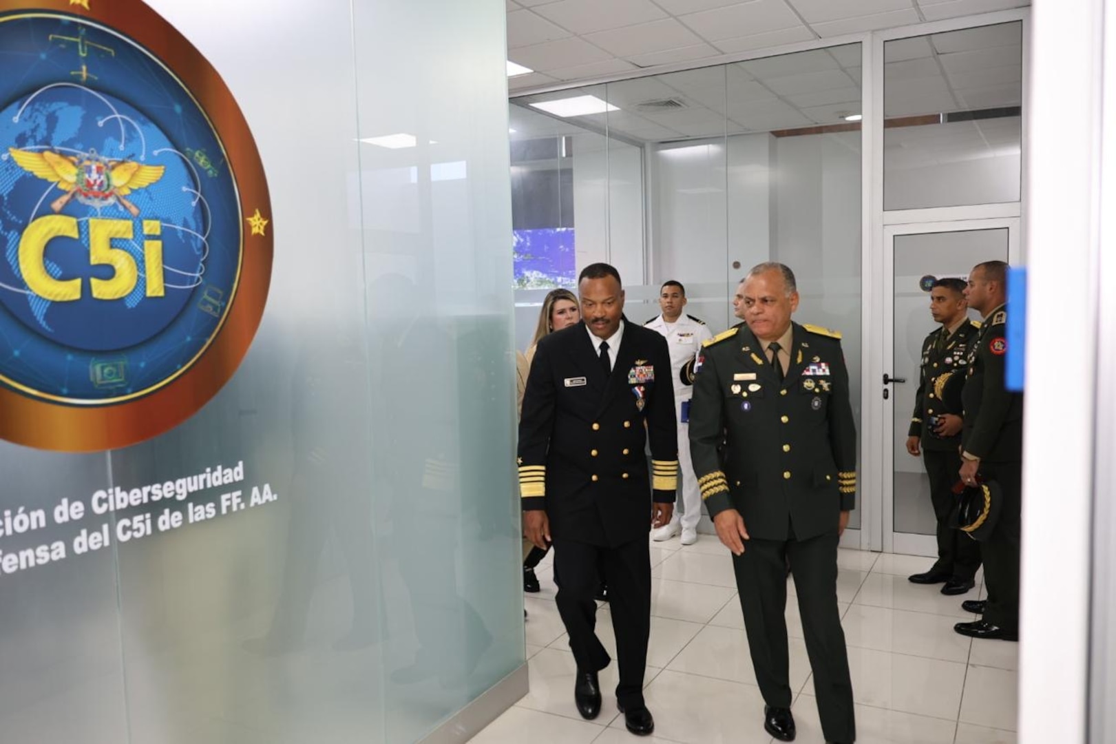 Two men in black military uniforms walk in a hallway.