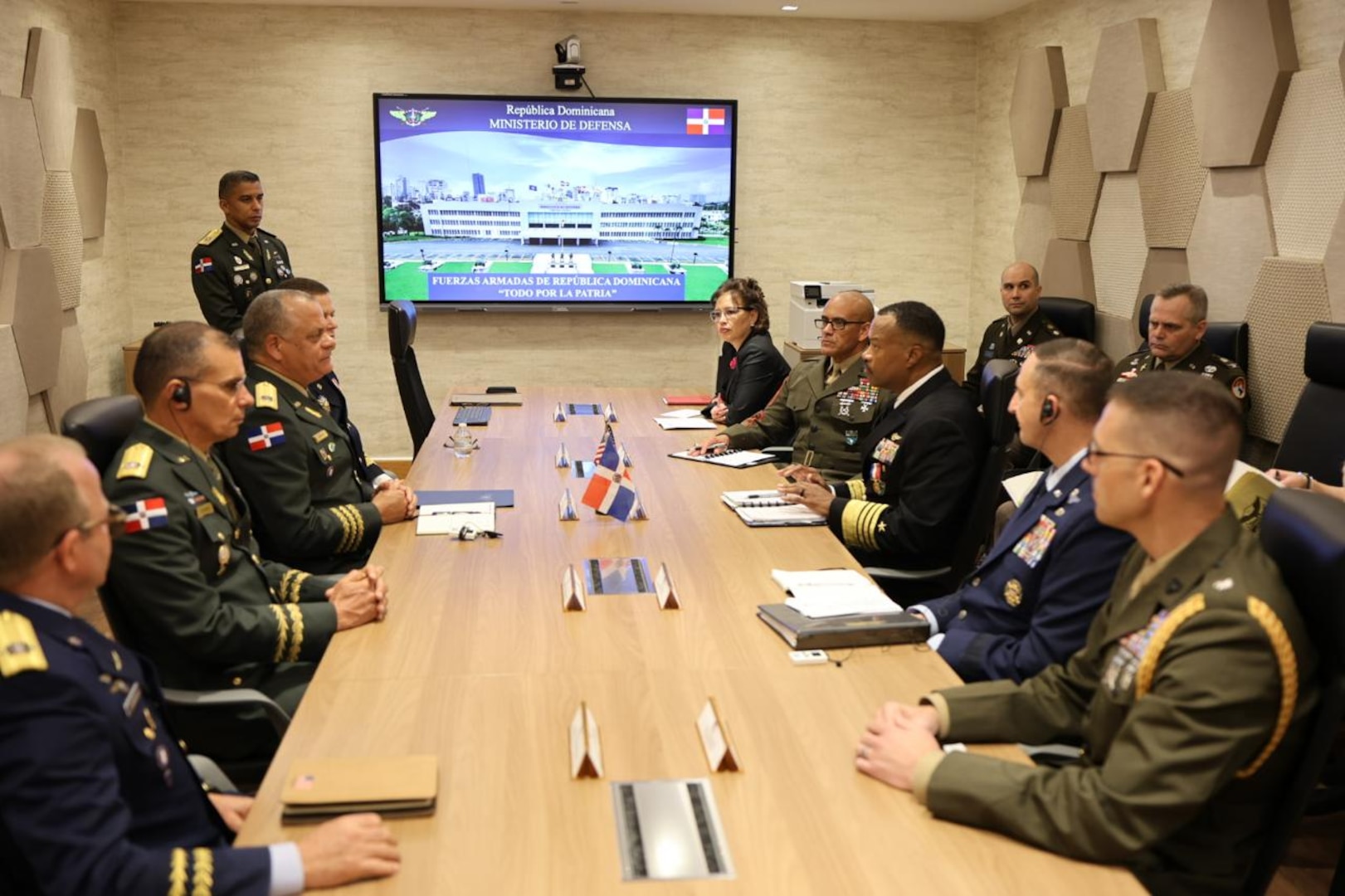 Military personnel in uniform sit around a long table during a meeting.
