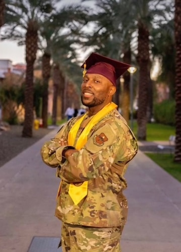 A man dressed in military uniform crosses his arms with a graduation cap and stole.