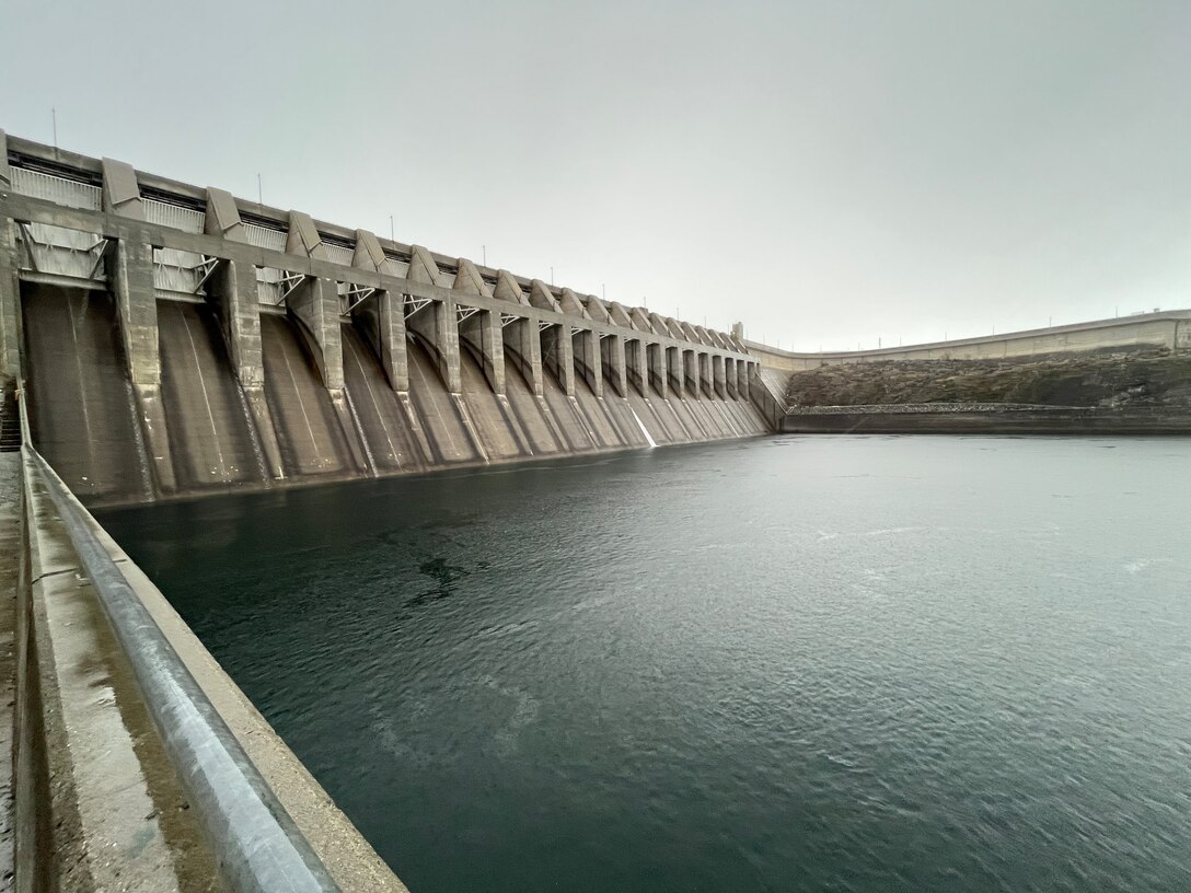 A view of the concrete spillway of a dam with the Columbia River in the foreground.