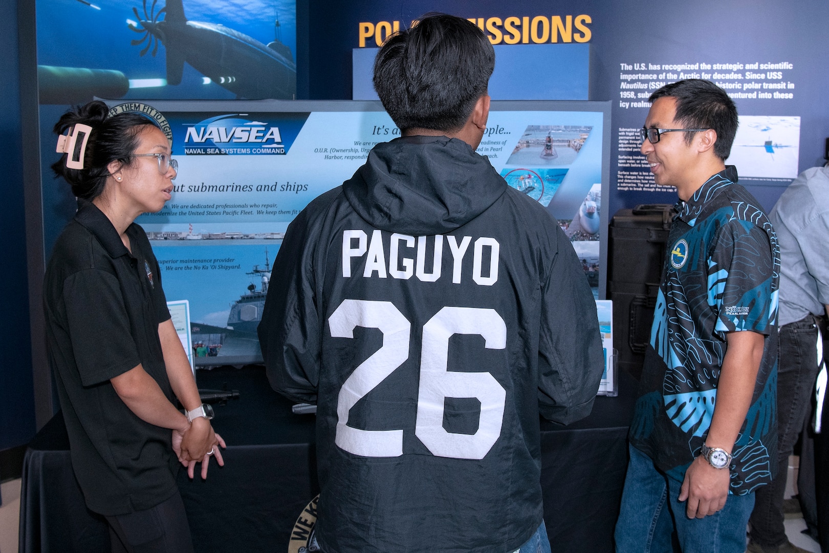 Engineers Traci Sunada and Malcolm Menor from the Pearl Harbor Naval Shipyard and Intermediate Maintenance Facility talk with a student from Honolulu Community College CTE Academy during a community event at the Pacific Fleet Submarine Museum July 15, 2025.