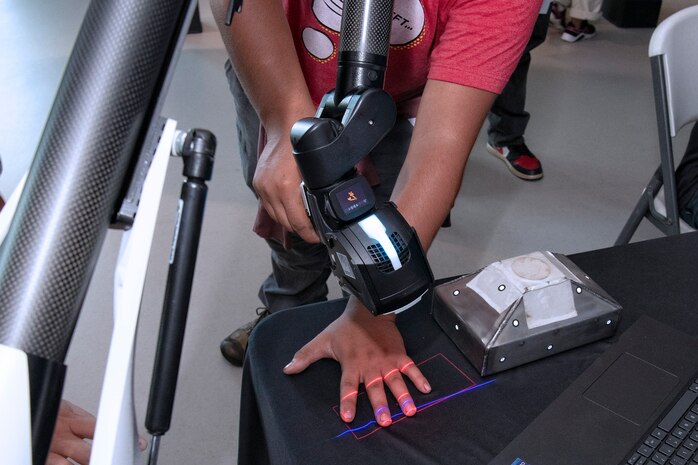A student from the Honolulu Community College CTE Academy scans his hand with a laser scanner from the Pearl Harbor Naval Shipyard and Intermediate Maintenance Facility sheet metal shop during a community event at the Pacific Fleet Submarine Museum July 15, 2025.