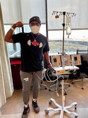 A man stands and flexes his arm next to medical equipment.