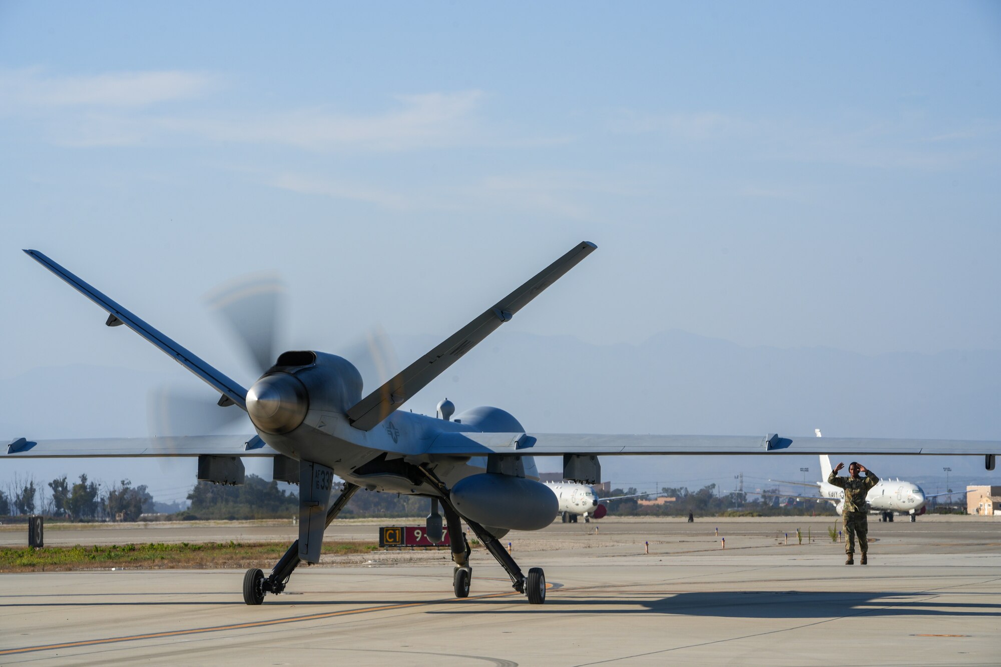 A man in a military uniform marshals an MQ-9 Reaper.