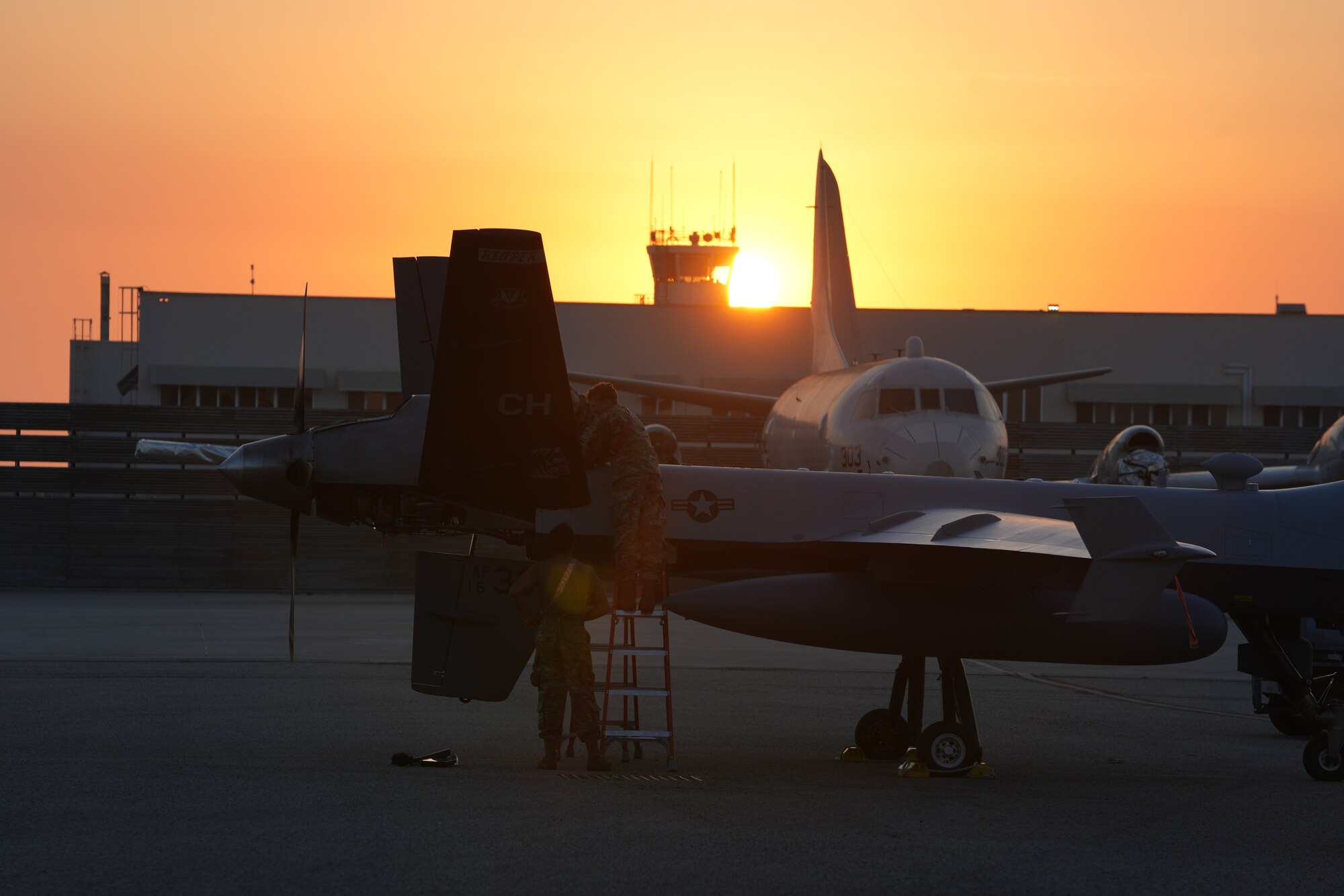 Three men in military uniforms perform maintenance on an MQ-9 Reaper.