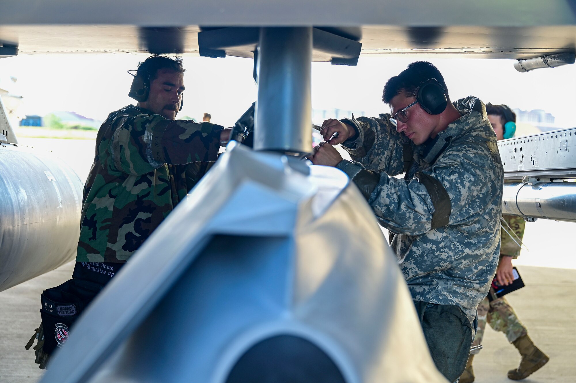 Two men use tools on a munition.