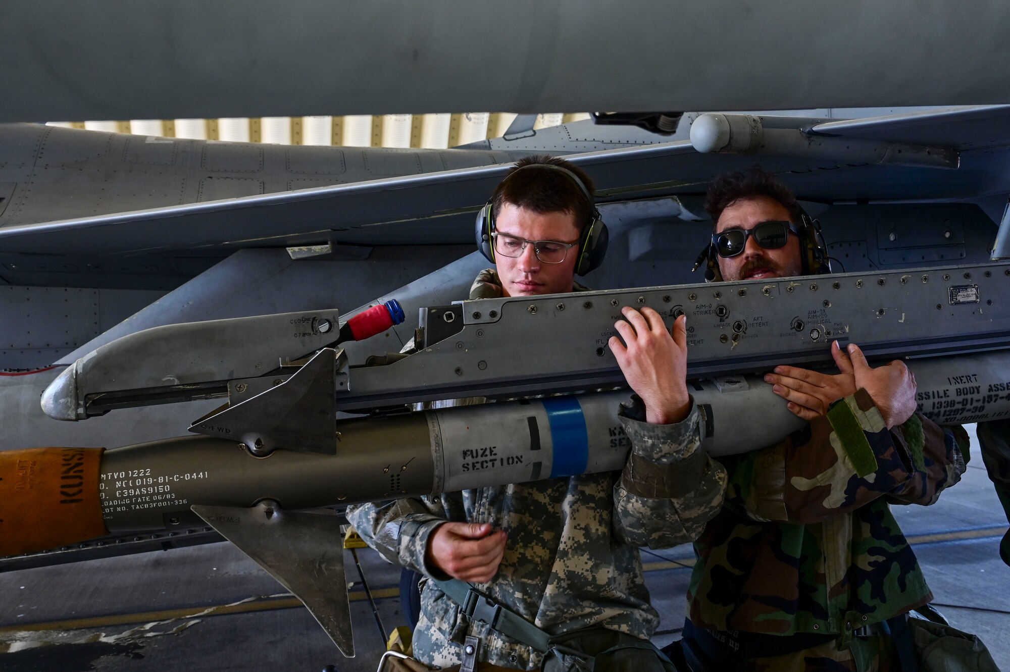 Two men lift a munition.